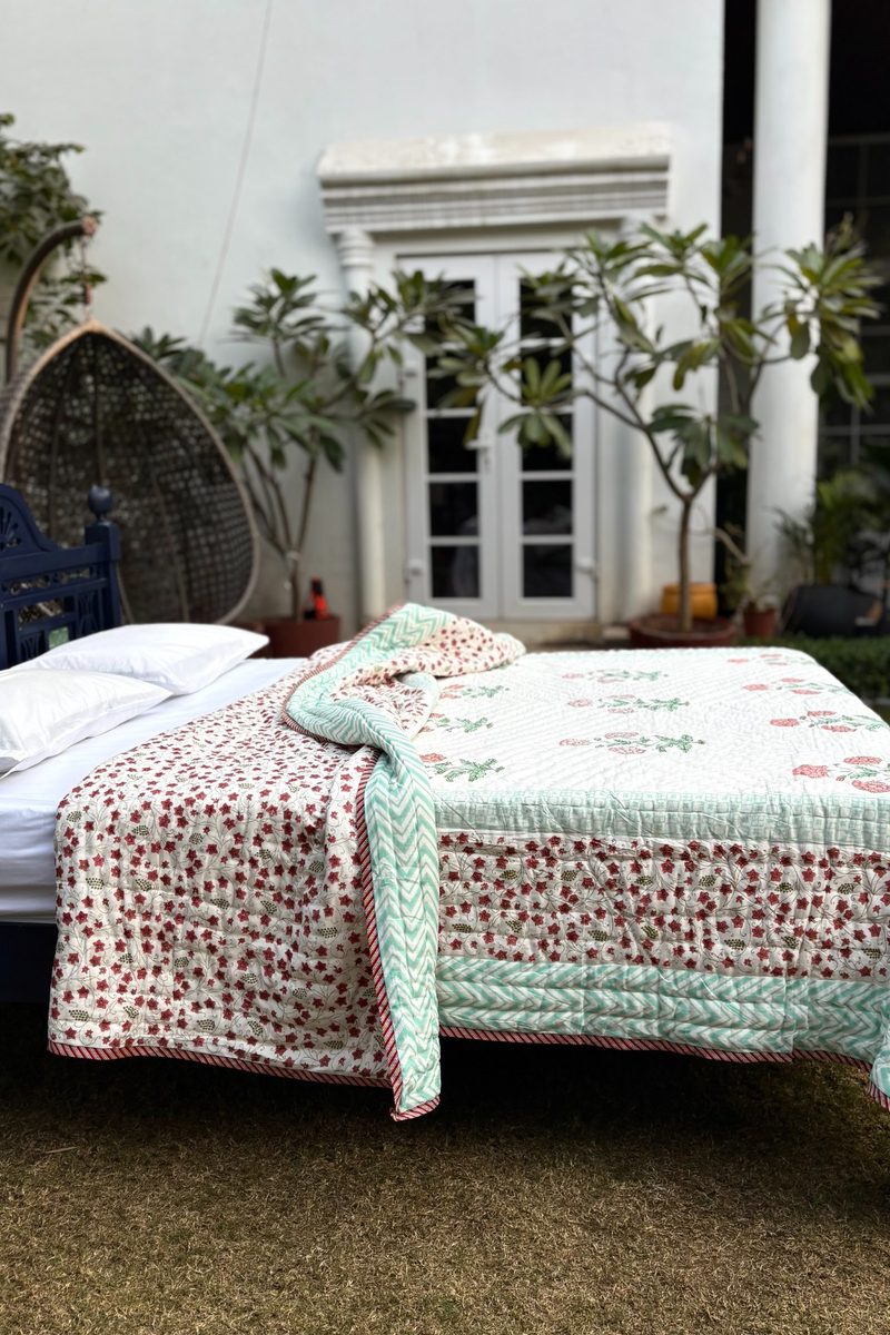 Handcrafted block print quilt with floral pattern and mint green chevron border, premium cotton bedding styled outdoors