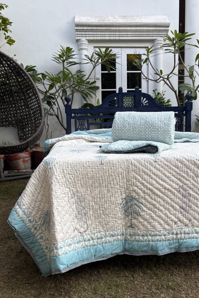 Aqua blue and ivory hand block printed cotton quilt set with palm tree and leopard motifs, styled on outdoor garden bed