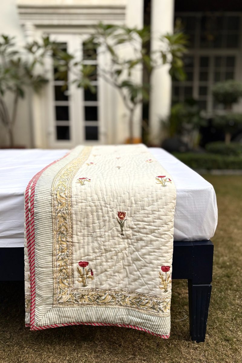 Close-up of hand block printed quilt fabric with red floral motifs, fine cotton quilting and soft cream background