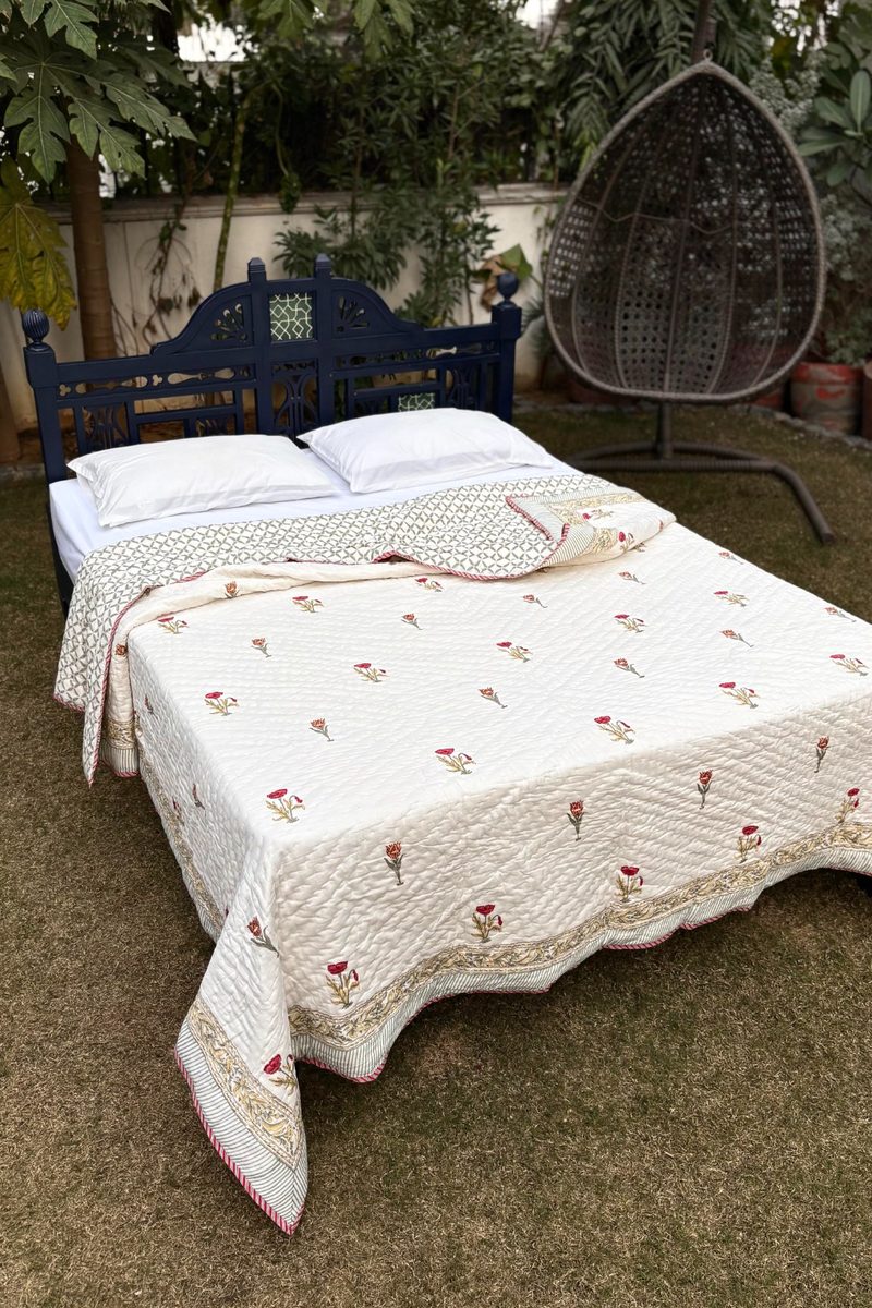 Hand block printed cotton quilt with delicate red floral motifs and quilted texture, styled folded on a bed