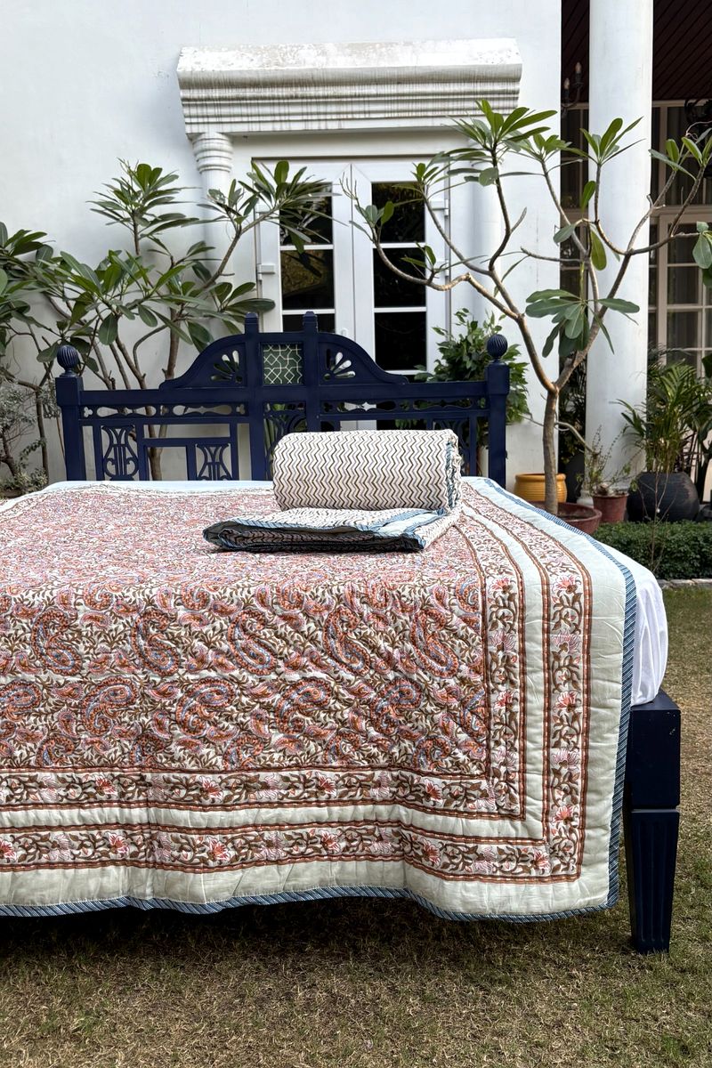 Hand block printed paisley quilt in rust and blue tones with floral border on ivory cotton base