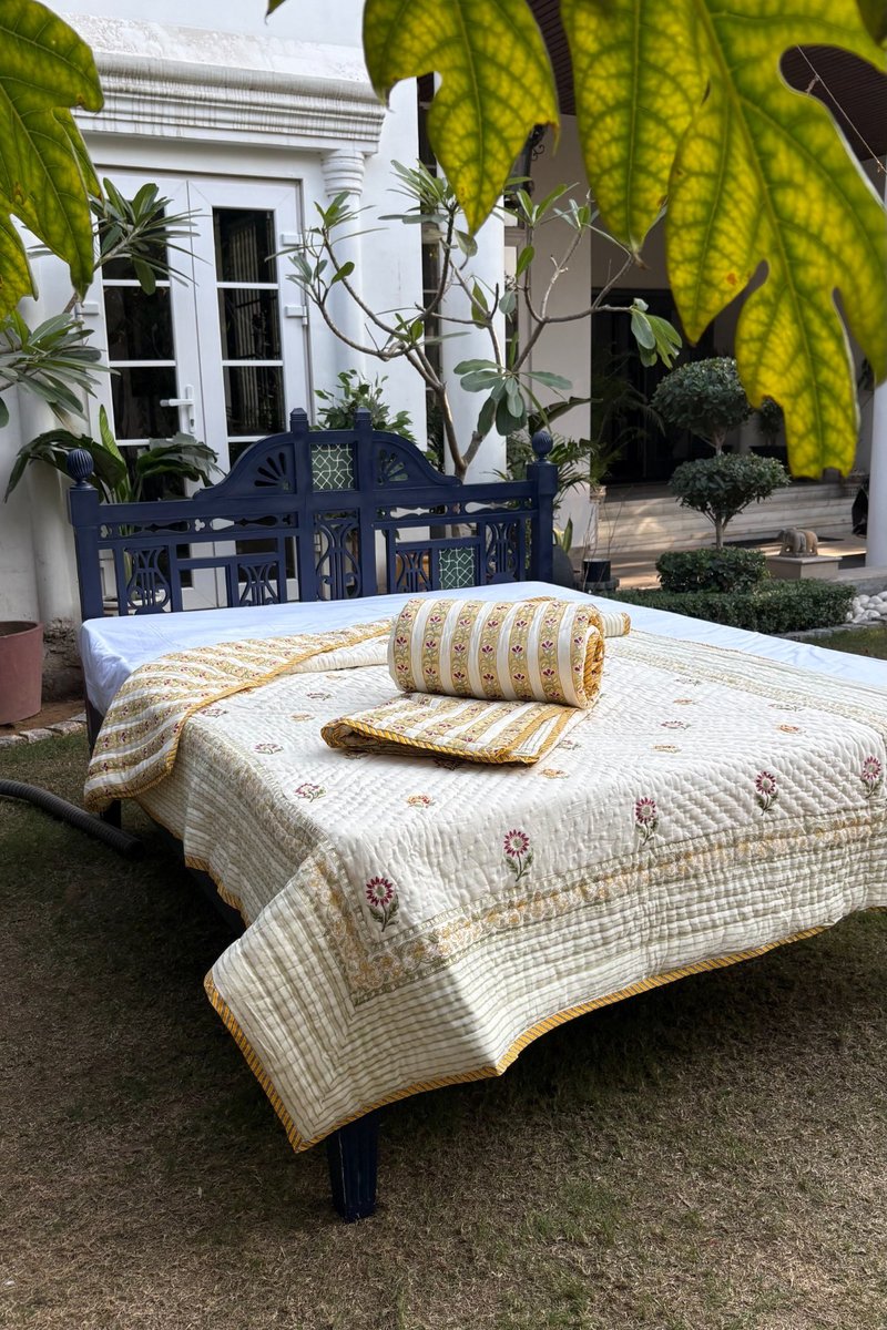 Ivory cotton quilt with pink floral motifs and yellow striped border displayed on garden bed