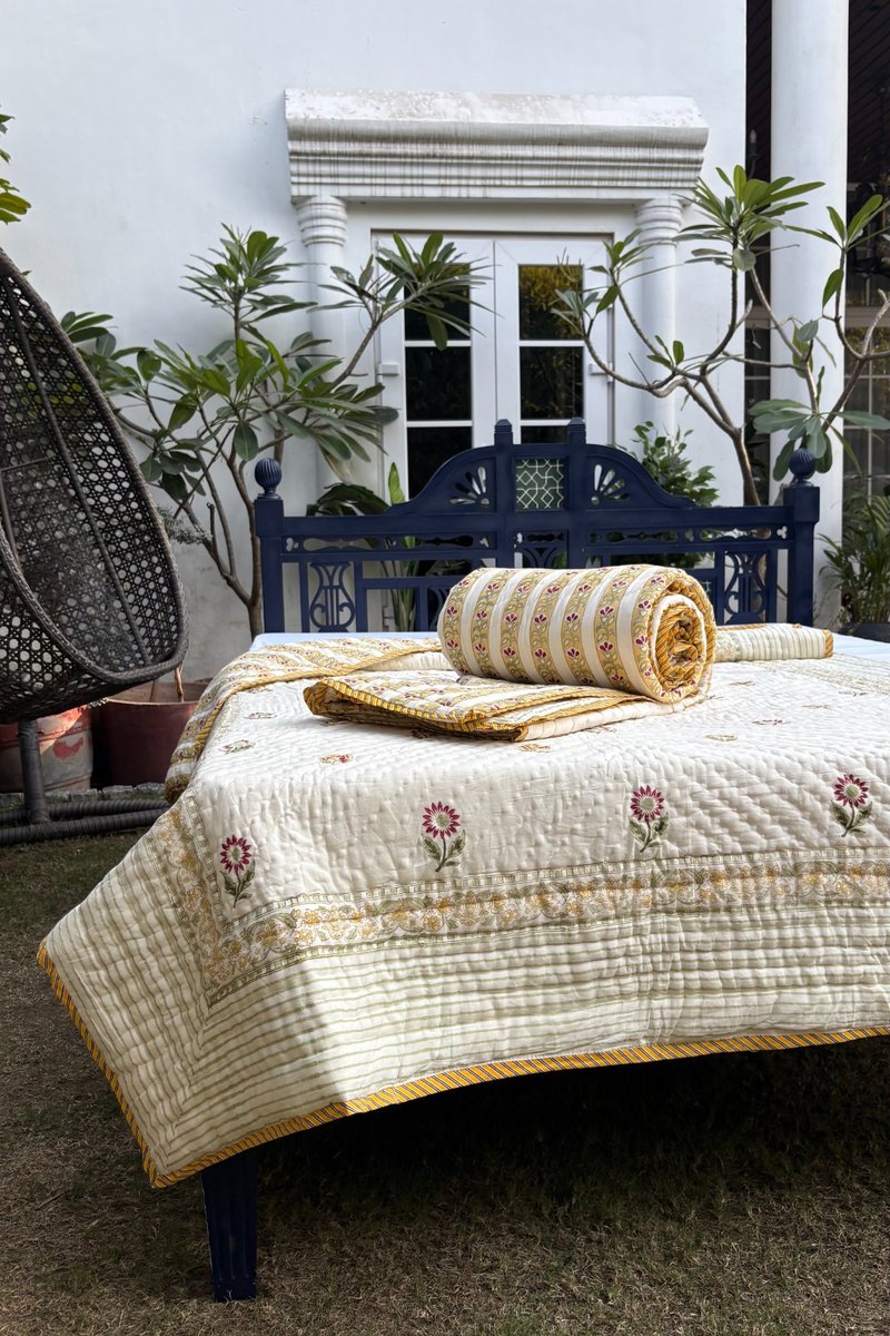 Ivory and mustard floral cotton quilt set styled outdoors on navy wooden bed with garden backdrop