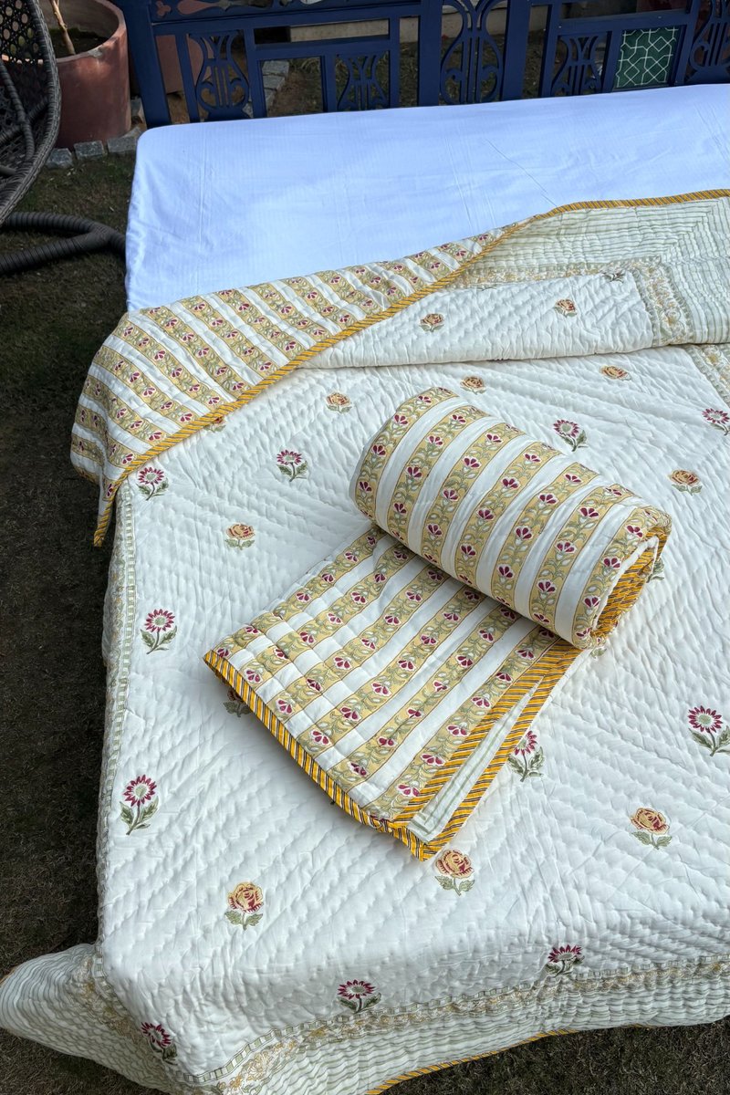 Handblock floral quilt in ivory and saffron tones with striped border styled in outdoor garden setting