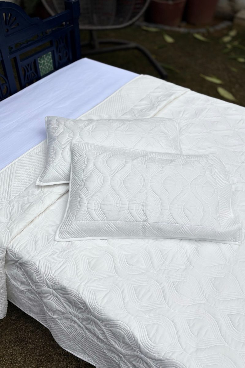 Ivory cotton quilt with all-over hand quilting, displayed on a blue wooden bed in a garden setting