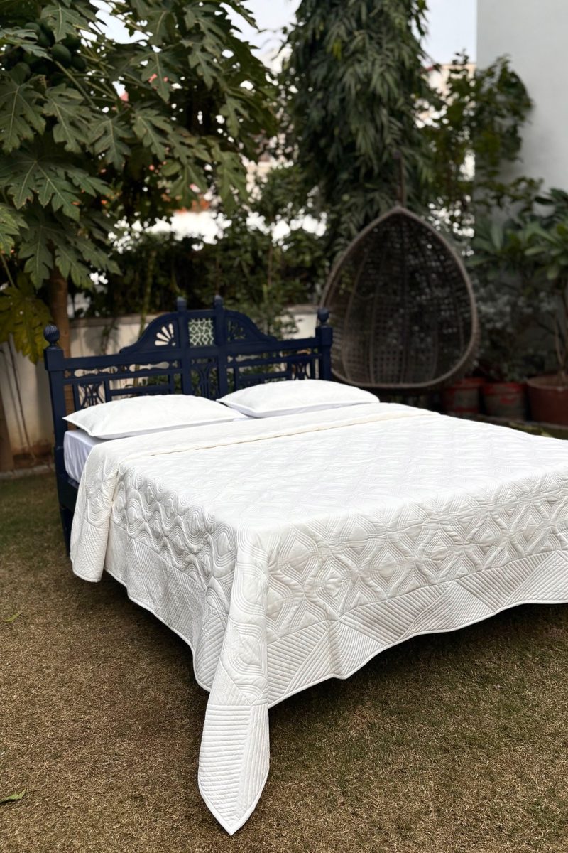 Minimal ivory quilted bedcover with diamond stitch pattern, styled in an outdoor garden bedroom