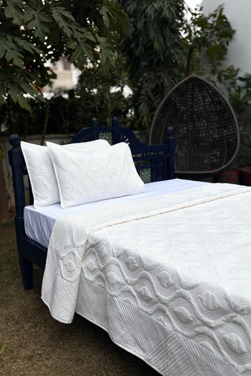 Solid hand-quilted cotton bedspread with textured geometric stitching, styled outdoors on a wooden bed