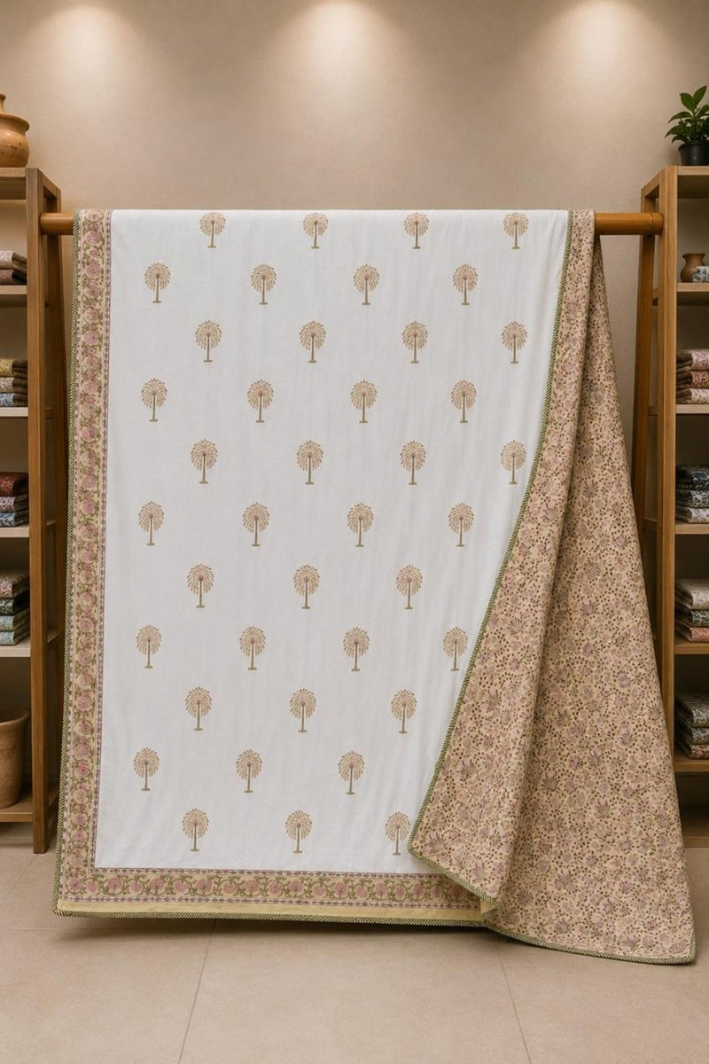 A white cotton dohar with a repeating tree pattern and a floral border, draped over a wooden stand in a warm, neutral-toned room.