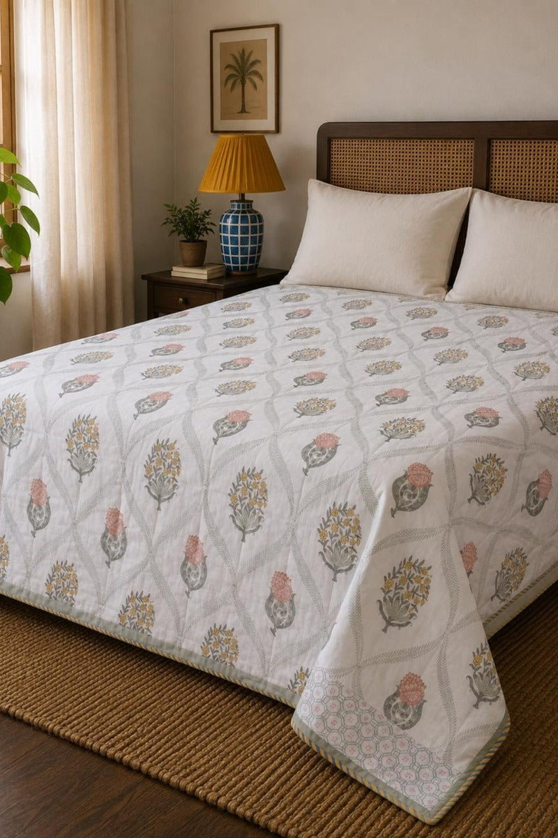 Cotton Dohar with a repeating floral block print in muted pink, blue, and gold, styled on a bed in a warm, neutral-toned bedroom.