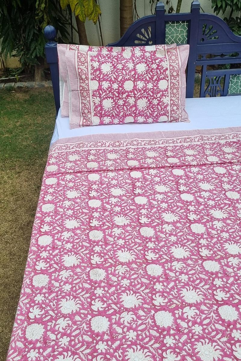 Hand block printed pink cotton bedsheet with white floral motifs and decorative border spread on double bed in outdoor garden