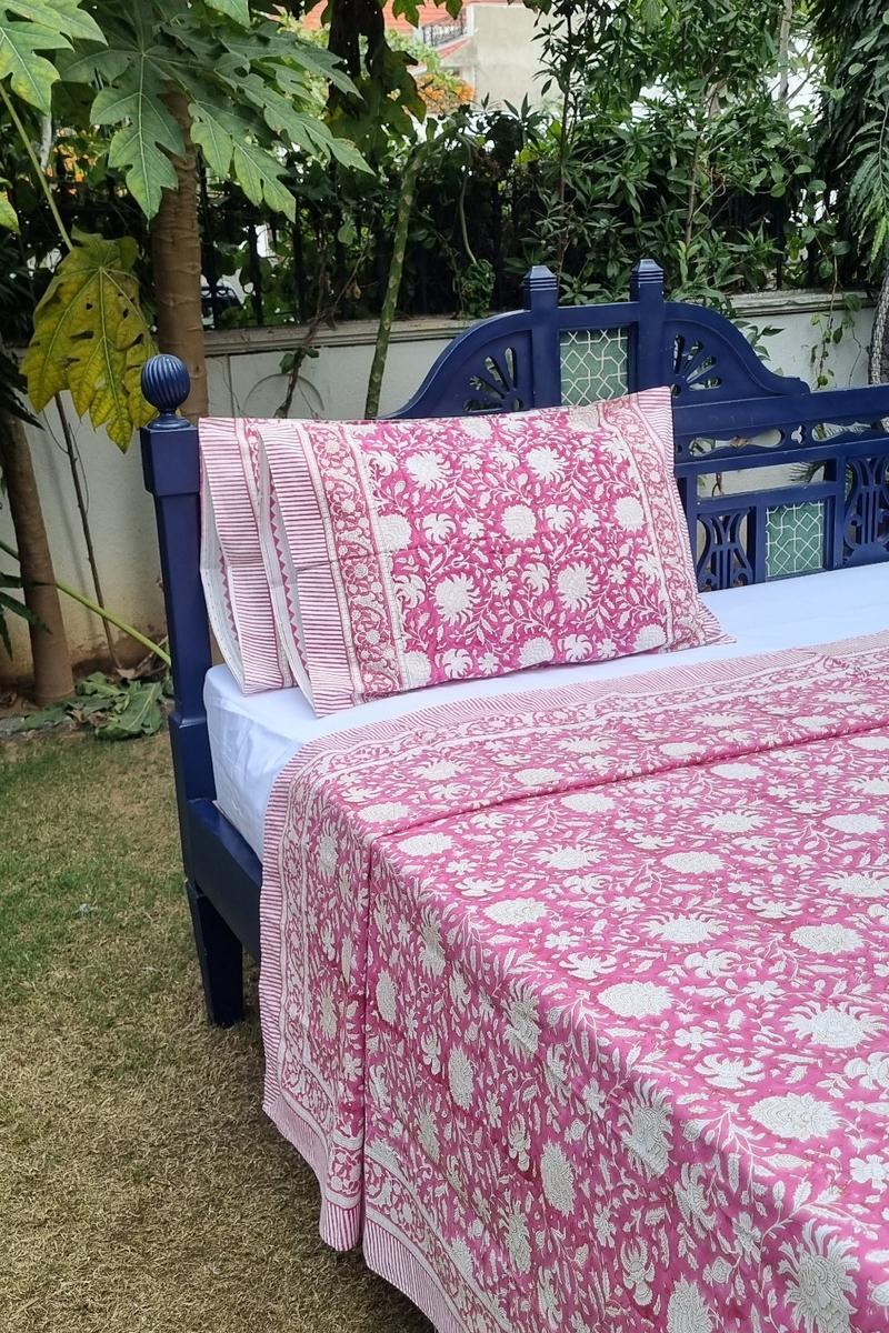 Pink Mughal floral print cotton bedsheet with matching pillow covers and striped hem border on traditional wooden bed