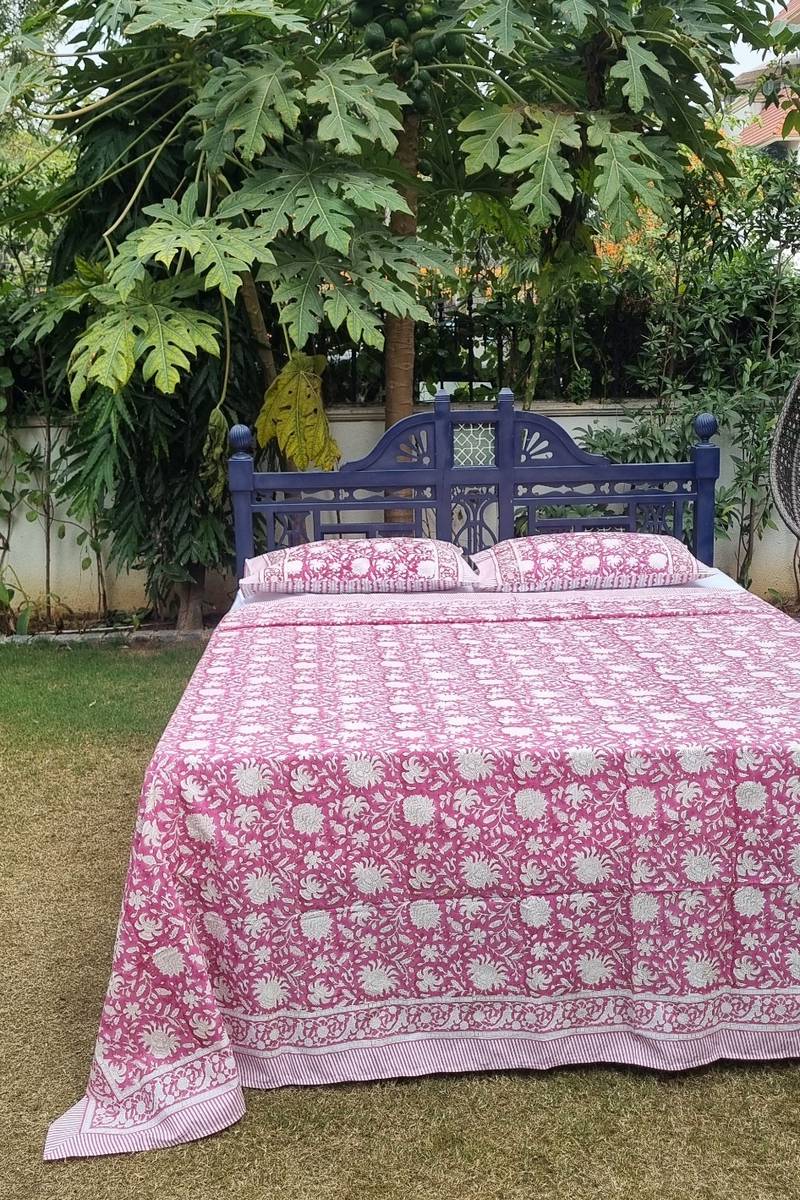 Pink and white floral hand block printed cotton bedsheet with striped border and matching pillow covers displayed on outdoor wooden bed